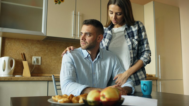 Woman comforts man at kitchen table with food